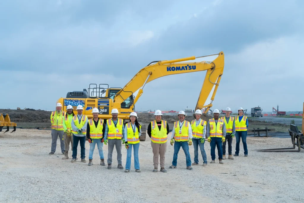 Project staff pose in front of the Hybrid excavator.